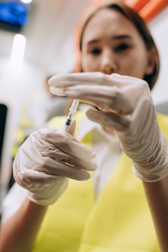 A paramedic wearing gloves prepares a syringe indoors, focused on medical care.